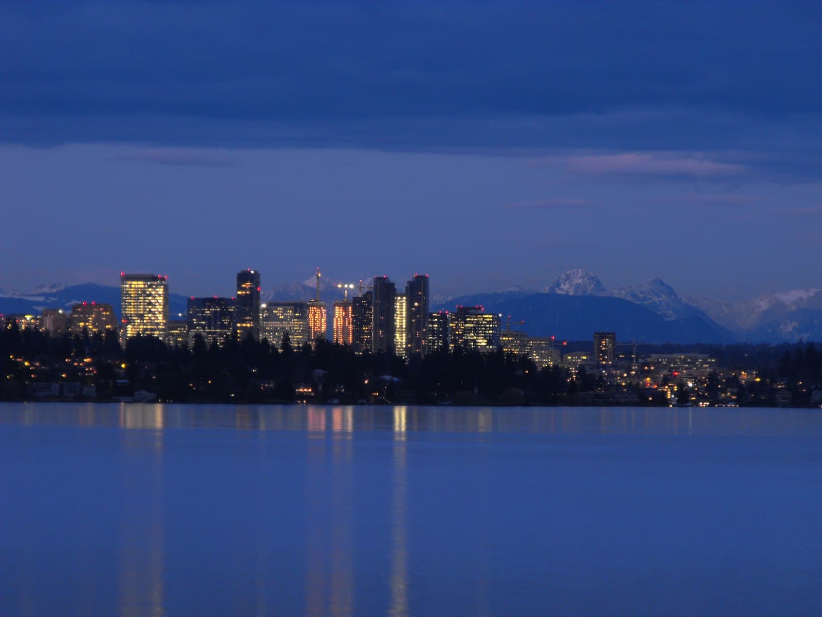 Downtown Bellevue skyline across Lake Washington at dusk, with the Cascades behind